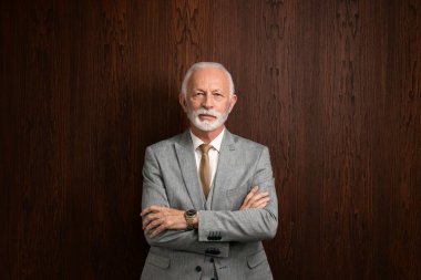 Ofisinde kollarını kavuşturmuş vaziyette duran kendinden emin ve kararlı bir iş adamı portresi..