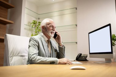 Kıdemli işadamı rahat bir ofiste oturuyor ve telefon görüşmesi yapıyor..