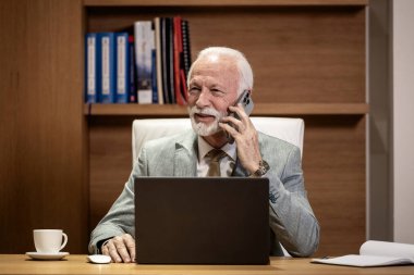 Kıdemli işadamı rahat bir ofiste oturuyor ve telefon görüşmesi yapıyor..
