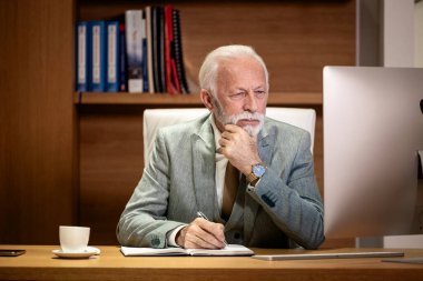 Lüks ofisin kıdemli müdürü bilgisayarda çalışıyor ve defterine notlar alıyor..