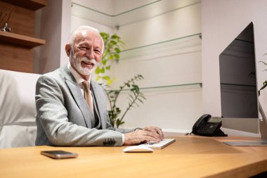 Lüks ofisinde oturan beyaz sakallı iş adamının portresi..