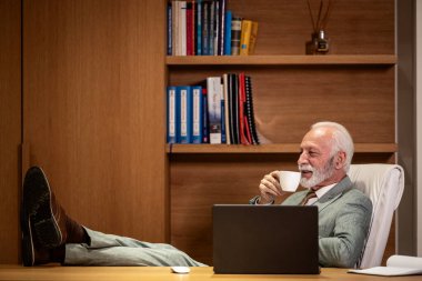 Kıdemli işadamı çalışırken kahve içiyor..