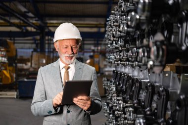 Fabrika üretim hattında duran zengin sanayi adamının portresi.