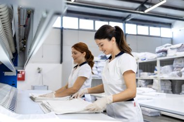 Kadın kuru temizleme çalışanları temiz çamaşırları katlıyor ve müşteri teslimatına hazırlanıyor..