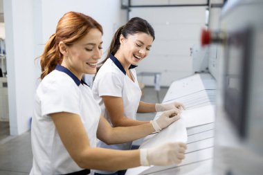 Beautiful laundry workers preparing bedsheets and pillowcases for industrial ironing machine. clipart