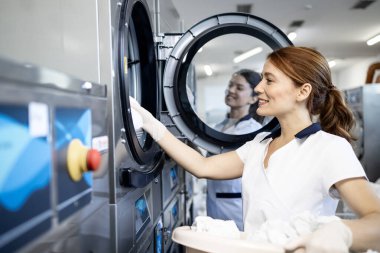 Kuru temizleme işçileri çamaşır makinelerini çamaşır makinesiyle dolduruyor.