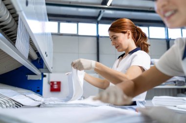 Female laundry workers folding linen and bedsheets after ironing in dry cleaning service. clipart