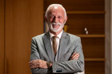 Ofisinde kollarını kavuşturmuş vaziyette duran kendinden emin ve kararlı bir iş adamı portresi..