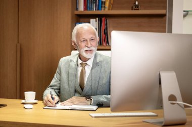 Ofiste çalışan kıdemli CEO mali sonuçları analiz ediyor ve ajandasına not alıyor..