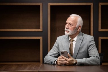 Başarılı ve varlıklı bir şirket müdürünün portresi lüks bir ofiste akıllı bir telefon tutuyor..