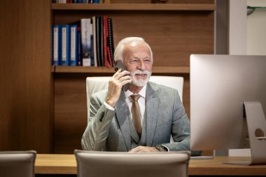 Kıdemli işadamı rahat bir ofiste oturuyor ve telefon görüşmesi yapıyor..