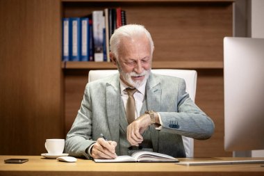 Konforlu rahat ofis içinde kıdemli yönetici saatini kontrol ediyor..