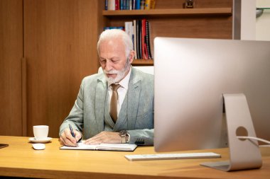 Ofiste çalışan kıdemli CEO mali sonuçları analiz ediyor ve ajandasına not alıyor..