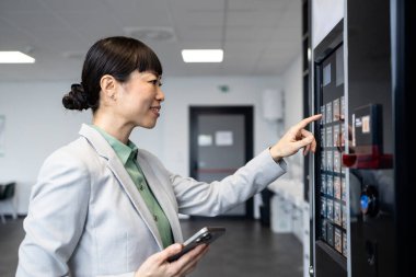 İş kadını, iş molasında otomattan abur cubur alıyor ve akıllı telefon aracılığıyla ulaşılamaz ödemeler yapıyor..