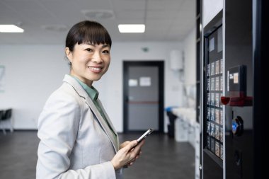 İş kadını portresi otomattan atıştırmalık alıyor iş molasında ve akıllı telefon aracılığıyla ulaşılamaz ödemeler yapıyor..