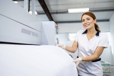 Kadın çamaşırcı ütü makinesine çarşaf geriyor..