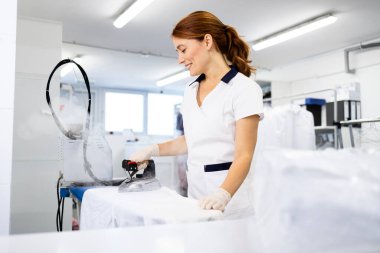 Kuru temizleme servisinde çamaşırları ütüleyen kadın çamaşırcı..