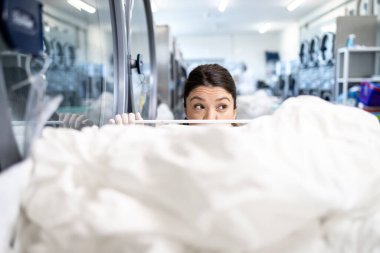 Çamaşırhanede dikilip kameraya bakan pozitif kadın işçinin portresi..