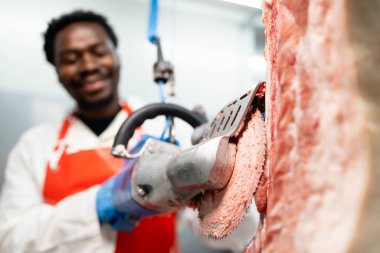 Yemek fabrikasında et işlemek için elektrikli testere kullanan mezbaha işçisi..
