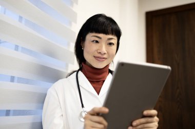 Beyaz önlüklü Japon doktor elinde tablet bilgisayarla hastanedeki hasta randevusunu kontrol ediyor..