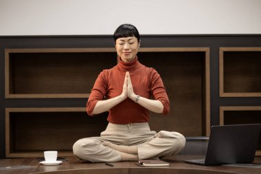 Yoga ofiste. Ofisteki masasında oturan Japon kadın yoga meditasyon egzersizi yaparak vücudunu rahatlatıyor..