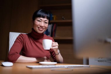 Güzel, gülümseyen bir kadın rahat ofisinde çalışmaktan zevk alır. Ofisinde bir fincan kahve olan Japon iş kadını..