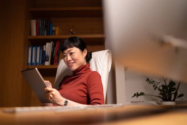 Güzel, gülümseyen bir kadın rahat ofisinde çalışmaktan zevk alır. Ofisinde tablet bilgisayarı olan Japon iş kadını..