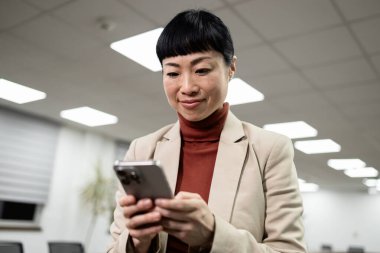 Şık takım elbiseli gülümseyen Japon kadın şirket toplantı odasında telefonunu kullanıyor..