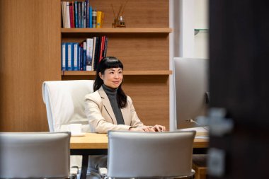 Gözlüklü güzel Japon iş kadını şirket ofisindeki masaüstü bilgisayarında çalışıyor..