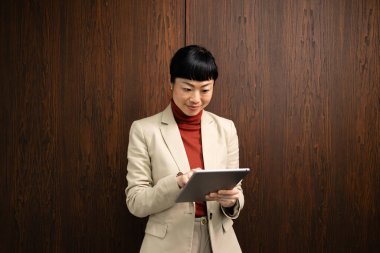 Şirket ofisindeki tablet bilgisayarda çalışan takım elbiseli kadın Japon yönetici..