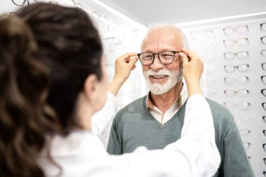 Tecrübeli bayan gözlükçü, optik mağazada yeni gözlük için mükemmel çerçeveyi seçmesine yardım ediyor..