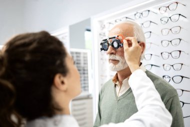 Tecrübeli kadın gözlükçü, optik mağazada üst düzey erkek görme yeteneği ve diyopteri test gözlüğü kullanarak test ediyor..