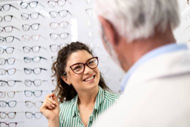Optik mağazasında yeni gözlük deneyen güzel, gülümseyen bir kadın deneyimli bir gözlükçüye danışıyor..