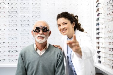 Deneyimli kadın gözlükçü, optik mağazada üst düzey erkek görme ve diyopter testlerini test gözlüğü kullanarak yapıyor..