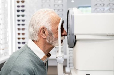 Optik mağazasındaki kıdemli adam görme duyusunu ve diyopterini otomatik kırıcı aletle test ediyor..
