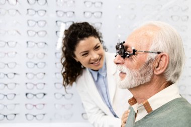 Profesyonel kadın göz doktoru ya da göz doktoru göz kliniğinde kıdemli erkek görme ve diyopter testleri yapıyor..