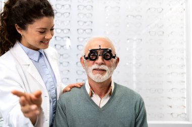 Uzman kadın optometrist kıdemli hastanın görüşünü kontrol etmek için diopter optik alet kullanıyor..