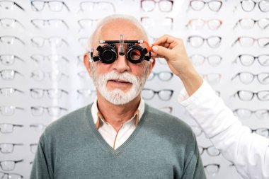 Uzman kadın optometrist kıdemli hastanın görüşünü kontrol etmek için diopter optik alet kullanıyor..