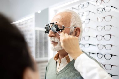 Üst düzey hastaların görüşlerini kontrol etmek için diopter optik cihaz kullanan kadın optometrist.