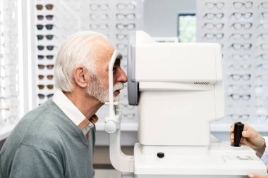 Optik mağazasındaki kıdemli adam görme duyusunu ve diyopterini otomatik kırıcı aletle test ediyor..