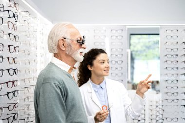 Tecrübeli bir optometrist, gözlük ve göz grafiği kullanarak kıdemli bir adamın görüş açısını, odaklanma ve diopterini kontrol ediyor..
