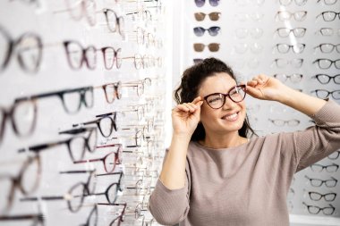 Güzel gülümseyen esmer kadın gözlük deniyor gözlükçüde.