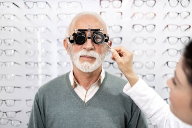 Göz kliniğinde gülümseyen kadın optometrist ve kıdemli hastanın portresi görüş muayenesine hazırlanıyor..