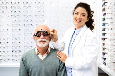 Göz kliniğinde gülümseyen kadın optometrist ve kıdemli hastanın portresi görüş muayenesine hazırlanıyor..