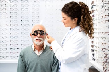 Tecrübeli bir optometrist, gözlük cihazı ve göz grafiği kullanarak üst düzey bir adamın görüş açısını, odaklanma ve diopterini kontrol ediyor..