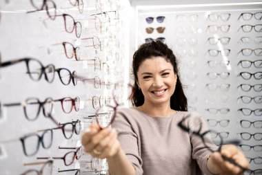 Güzel gülümseyen esmer kadın gözlük deniyor gözlükçüde.