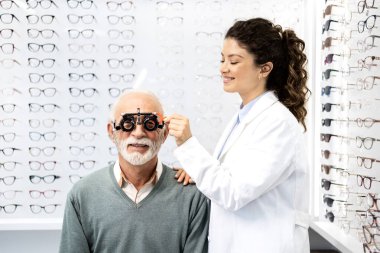 Kıdemli adam göz görüşünü test ediyor ve deneyimli optometrist ile diopter kullanıyor..