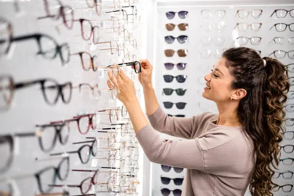 Güzel esmer kadın optik mağazasından şık gözlük çerçevesi seçiyor..