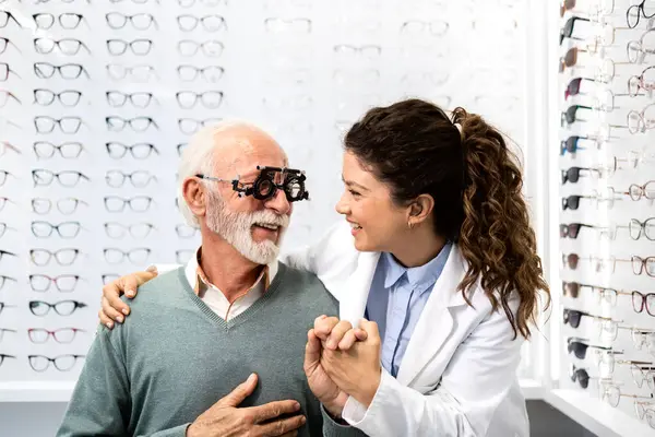 Profesyonel kadın optometrist kıdemli hastayla el ele tutuşuyor ve göz muayenesinden önce onu cesaretlendiriyor..