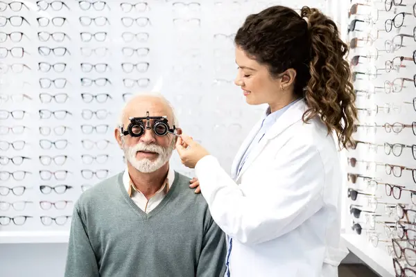 Tecrübeli bir optometrist, gözlük cihazı ve göz grafiği kullanarak üst düzey bir adamın görüş açısını, odaklanma ve diopterini kontrol ediyor..